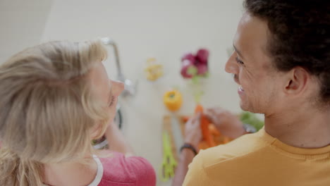 Happy-diverse-couple-preparing-and-washing-fresh-vegetables-in-kitchen,-slow-motion