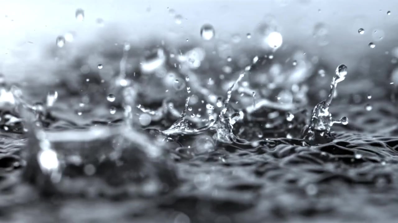 Primo piano al rallentatore di gocce di pioggia che schizzano sulla superficie dell'acqua