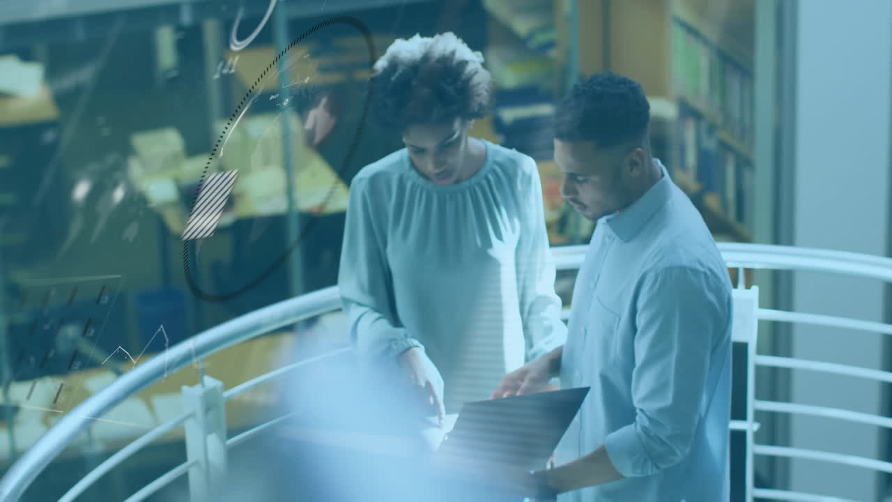 Two colleagues analyzing business data on laptop in office mezzanine, with floating data overlays