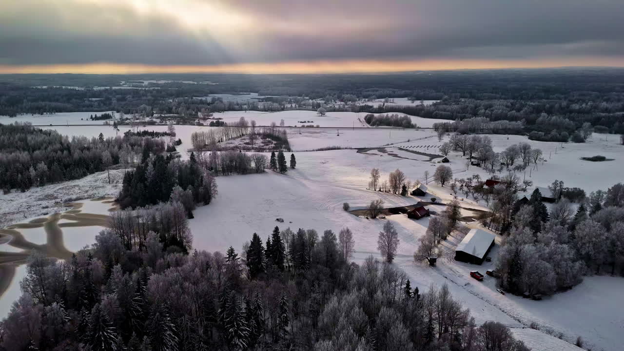 Vista aerea invernale da sogno di terreni agricoli ghiacciati, stagni ghiacciati ed edifici rurali sparsi sotto un cielo suggestivo con una soffusa luce solare che filtra tra le nuvole