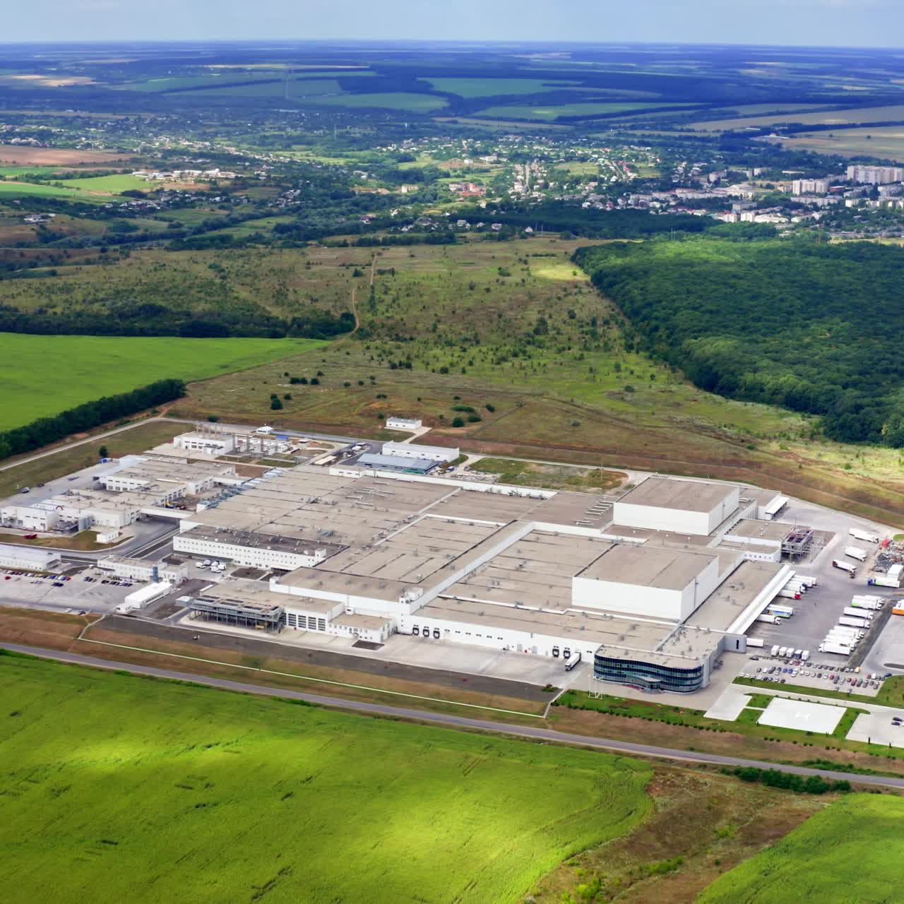 Aerial view of modern industrial building surrounded by green fields. Large modern production plant