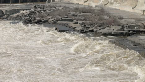 Panning across the rocky shore and raging waters of the Ottawa River to reveal the Hydro electric dam and the heritage power generation buildings on Chaudière Island in Ottawa, Ontario