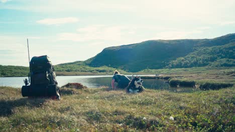 backpacker man with pet dog drink water from the lake