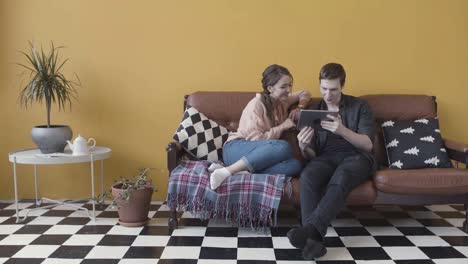 couple relaxing on a couch, looking at a tablet