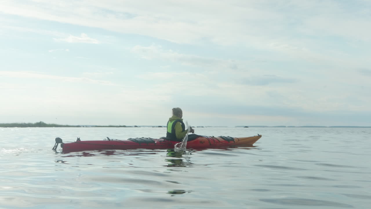 joven mujer rubia remando en un kayak del mar rojo en el mar abierto en finlandia, vaasa, archipiélago, hermosa atmósfera de atardecer de verano, tiro ancho