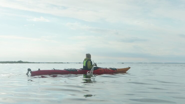 Young Blonde Woman Paddling in a Red Sea Kayak on the open Sea in Finland, Vaasa, Archipelago, Beautiful Summer Sunset Atmosphere, Wide Shot