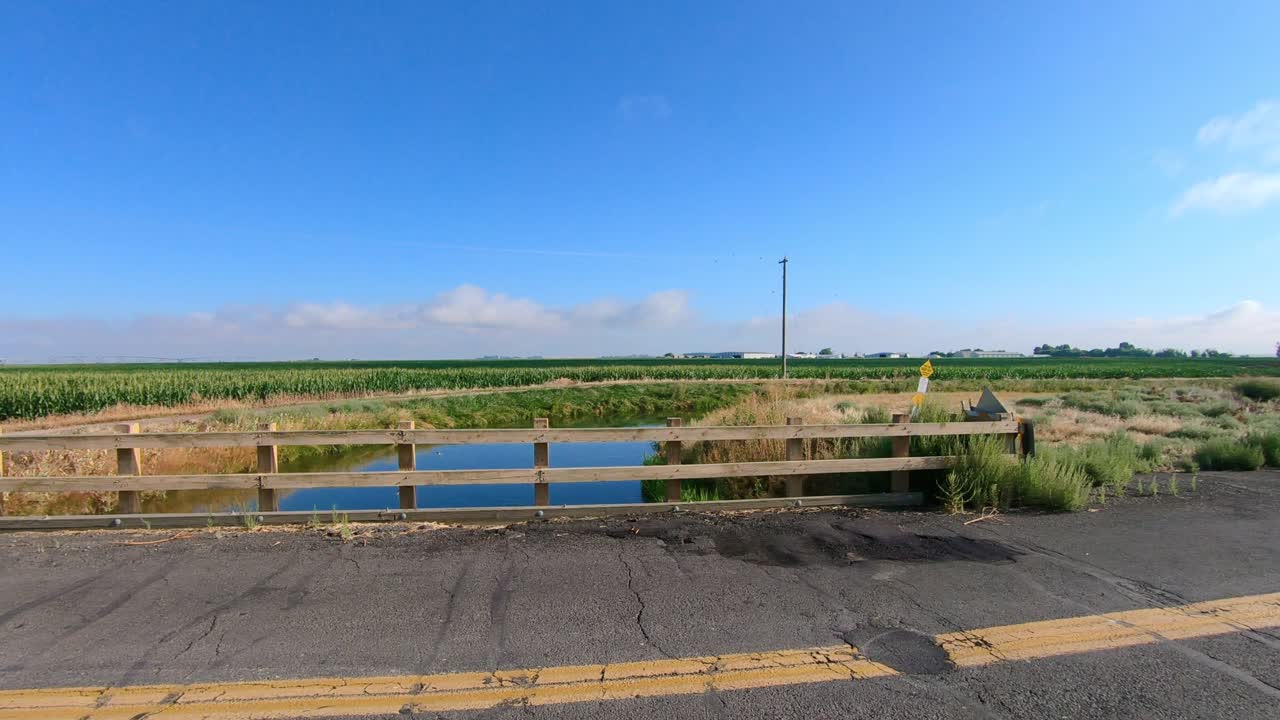 Pan of bridge over an irrigation canal; Visible are a corn and alfalfa fields in the background