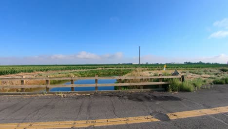pan of bridge over an irrigation canal; visible are a corn and alfalfa fields in the background