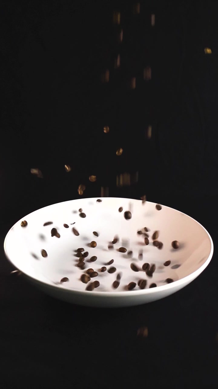 Chicchi di caffè tostati aromatici che cadono con grazia in un piatto di ceramica bianco su uno sfondo nero solido, mettendo in mostra la qualità e la freschezza dei chicchi di caffè premium.