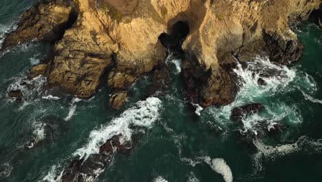 Drone-shot-of-California's-rocky-shoreline-with-waves-eroding-the-land