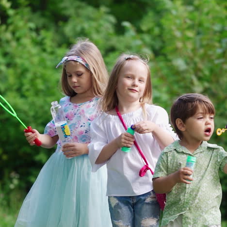 children with bubble blower in their hands over the nature background. two little girls and a cute small boy are blowing bubbles in the park.