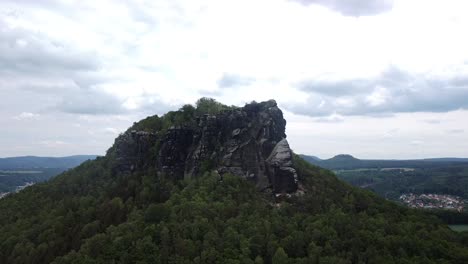 Drone-closing-in-on-a-famous-mountain-rock-formation-in-central-europe-with-forest-and-clouds