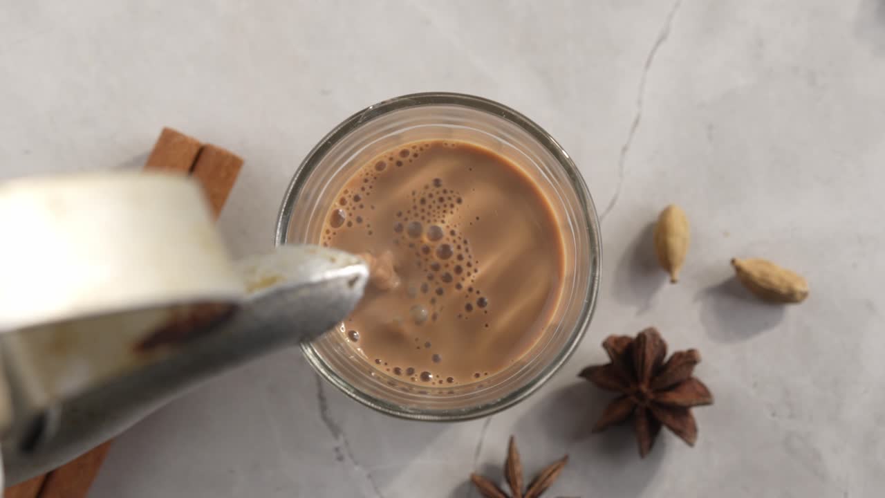 Chai indiano servito in tazze di vetro, preparato in un bollitore di metallo con masalas aromatici. Viene versato nel vetro.