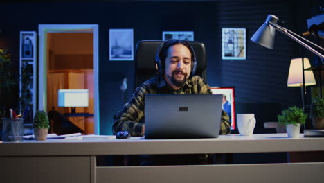 Cheerful-man-relaxing-at-home-by-watching-TV-show-on-laptop-using-headphones