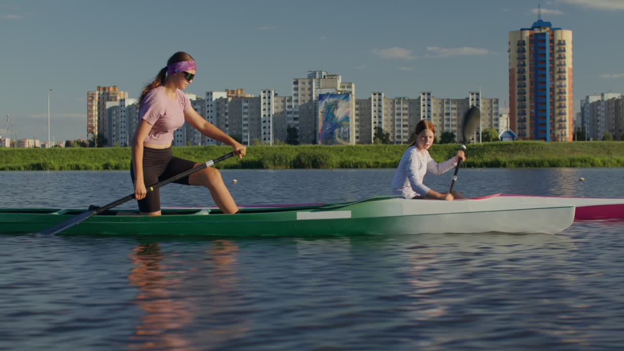 Due donne che vanno in kayak su un lago con edifici cittadini sullo sfondo