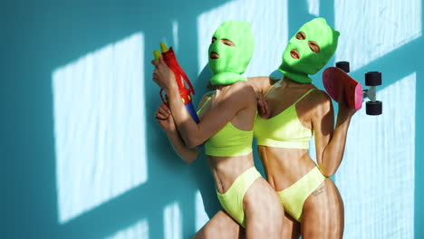 two women in neon swimwear and masks with water guns and skateboards