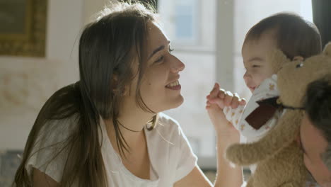 padres felices en la cama el domingo por la mañana jugando con su linda niña que sostiene un oso de peluche 1