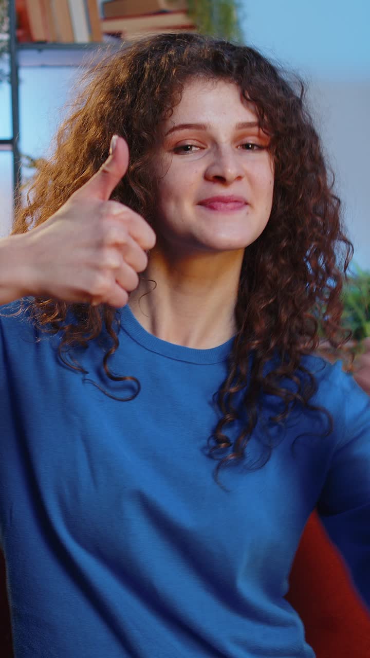 Mujer feliz mostrando los pulgares con las manos gestando como una aprobación positiva mirando a la cámara en casa