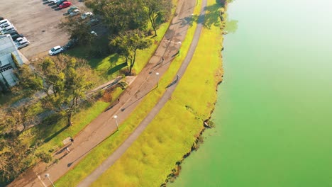 Cyclist-riding-on-Parque-Barigui-followed-by-drone-aerial-view,-Curitiba,-Paraná,-Brazil