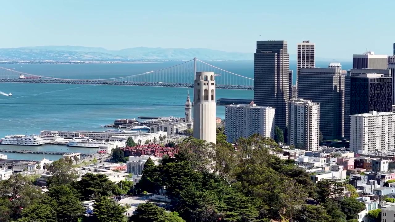 Luftfoto med drone av Coit Tower med utsikt over San Francisco Bay Bridge og sentrums silhuett i dagslys.
