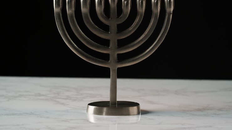 Tilt shot of Jewish menorah candelabrum with lit candles on a grey marble surface, against black background