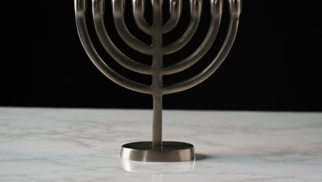 tilt shot of jewish menorah candelabrum with lit candles on a grey marble surface, against black background