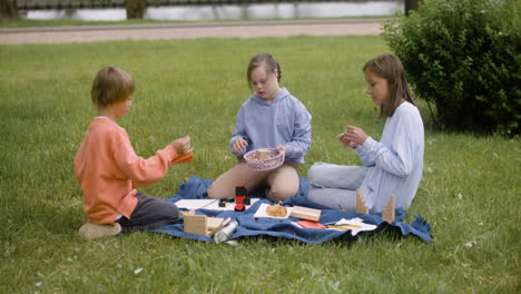 Kleines-Mädchen-Mit-Down-Syndrom-Sitzt-Mit-Ihren-Freunden-Im-Park.-Sie-Bauen-Holzmodelle