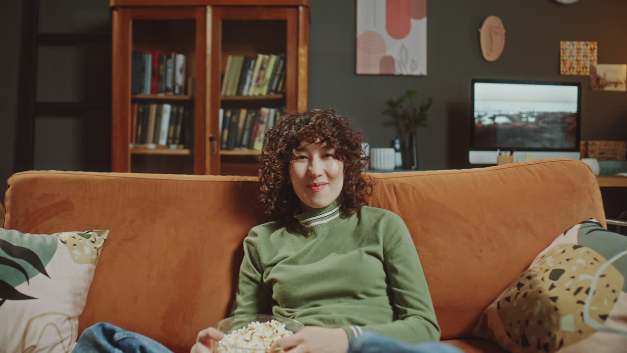 Portrait of Young Asian Woman Resting on Couch, Holding Popcorn and Smiling