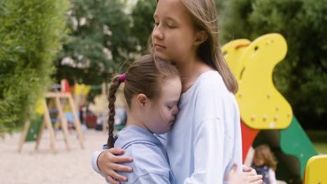 close-up view of a little girl with down syndrome hugging another girl in the park on a windy day