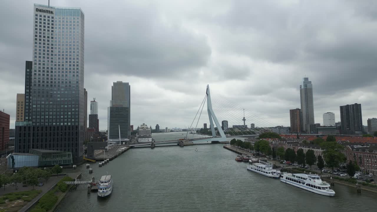 Aerial view of Rotterdam city skyline featuring the iconic Erasmus Bridge spanning the river under cloudy skies. Modern architecture and urban waterfront atmosphere