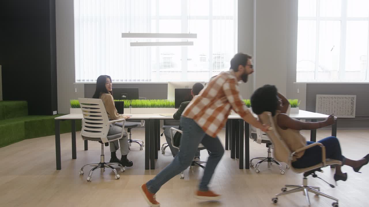 Man pushes African American woman in rolling chair in office