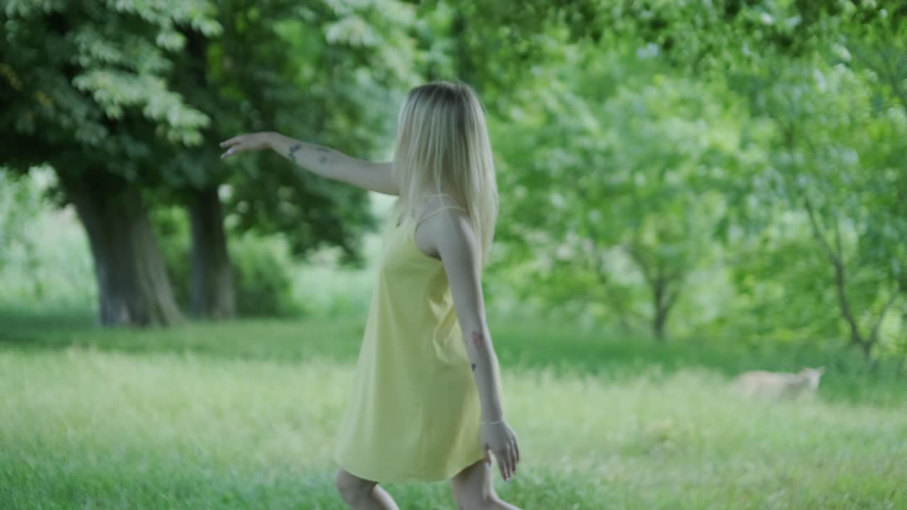 mujer con vestido amarillo bailando junto al árbol en el parque de verano