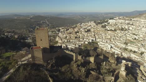 Aerial-shot-of-Yerda-Castle-in-gothic-style-on-a-steep,-rocky-hill,-Cazorla-city-with-white-houses-at-the-foot-of-the-mountain-and-olive-groves-at-the-distance