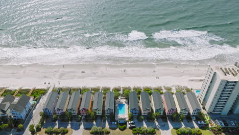 drone establishing shot of colorful hotel houses and swimming pool in front of beautiful surfside beach in south carolina during sunny day