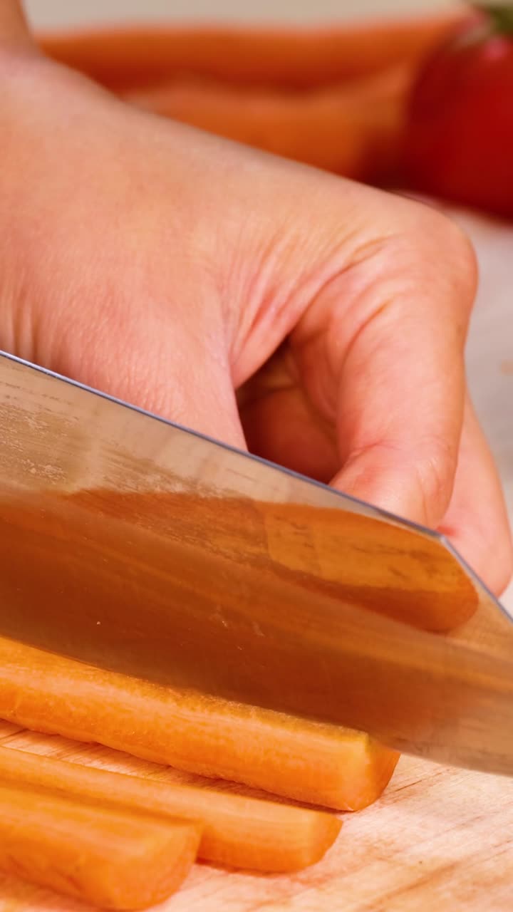 Extreme close-up of a chef's hands using a knife to slice carrots on wood