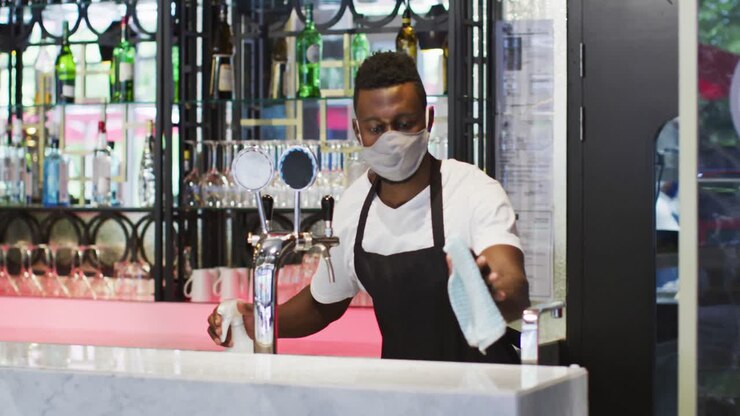 Barista afroamericano con mascherina che disinfetta la superficie del bancone