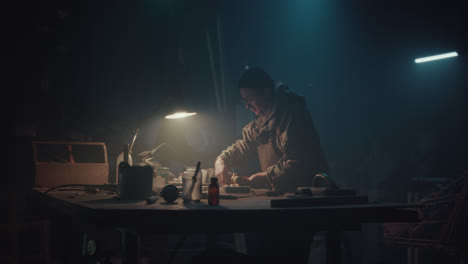 a bombmaker assembles a bomb in his workshop at night