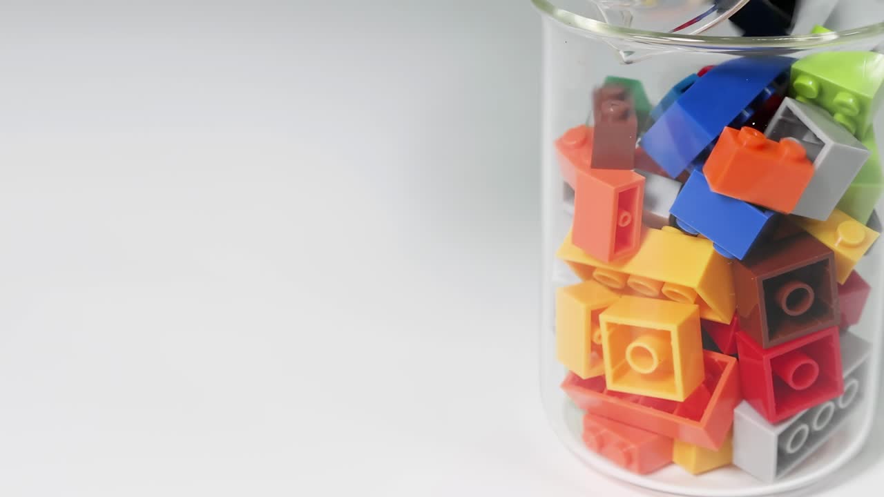 Hands pour vibrant building blocks into a clear glass container, showcasing a colorful assortment.