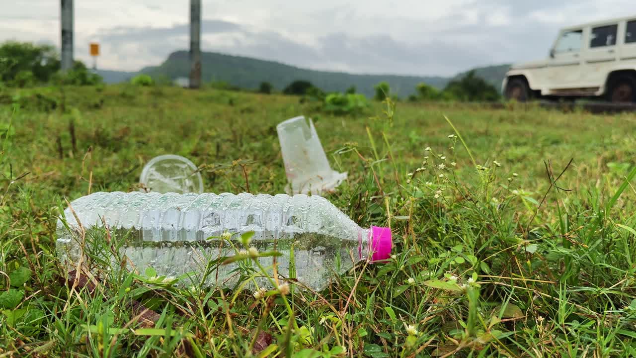 Low-angle shot showing discarded plastic bottle and cup on grass near a busy highway, highlighting littering, pollution, and environmental impact in rural India