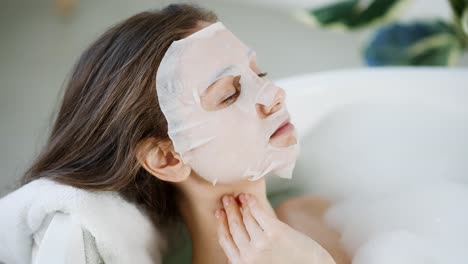 young woman with tissue face mask for skin care while laying in the bath