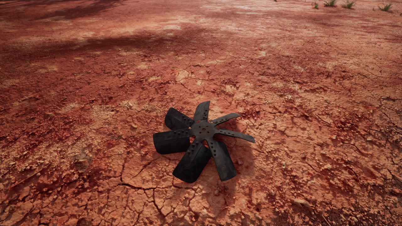 A black fan blade laying on cracked red dirt in the desert