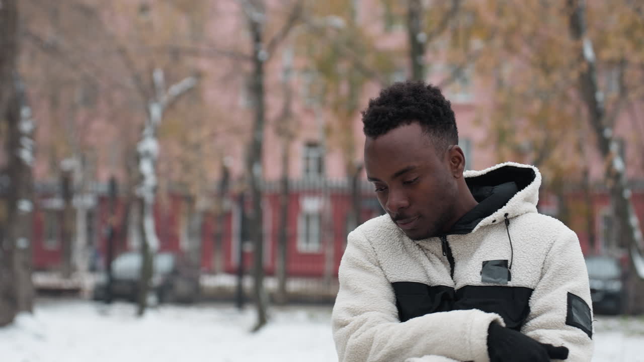 Zijaanzicht van een jonge man die kauwgom kauwt, zich klaarmaakt voor een buitentraining in een winterjas, gepositioneerd tegen een besneeuwde achtergrond, klaar om de trainingsapparatuur te gebruiken