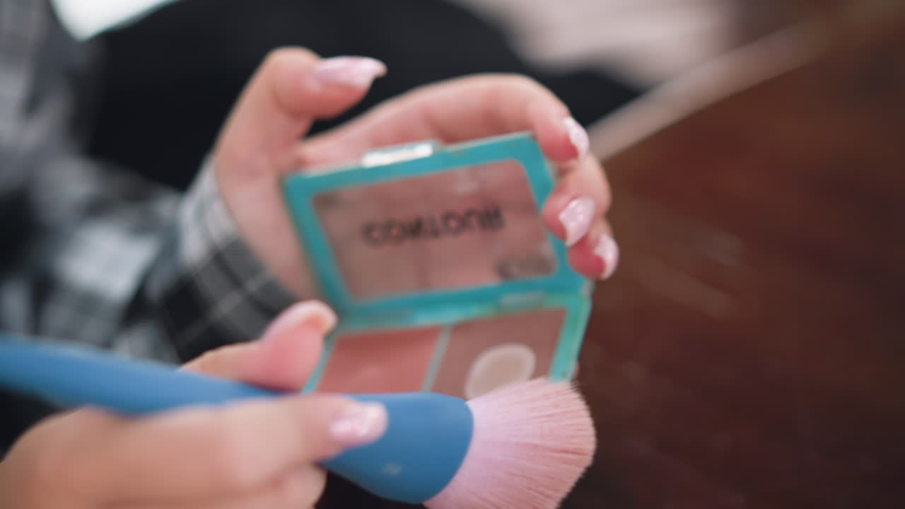 vista de cerca de la mano de la dama sosteniendo un cepillo de maquillaje suave, sumergiéndose suavemente en polvo compacto, uñas cuidadosamente cuidadas, y elementos esenciales de belleza en foco, creando un maquillaje estético y refinado