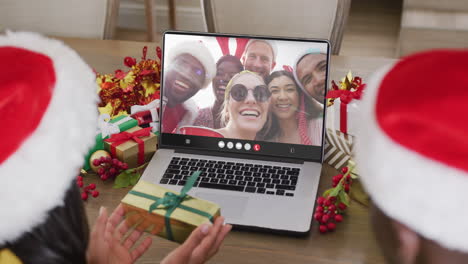 animación de una pareja diversa con sombreros de papá noel en una llamada de video portátil con amigos en navidad