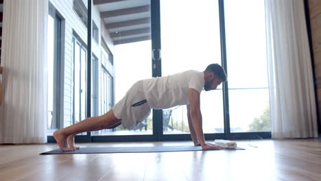 hombre biracial haciendo yoga y estiramiento en casa, cámara lenta