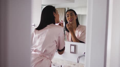 Mixed-race-gender-fluid-person-standing-in-bathroom-and-using-a-lipstick