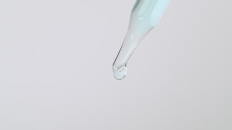 Close-Up-Of-Dropper-Pipette-Tip-With-Light-Blue-Liquid-Dripping-Isolated-In-White-Background