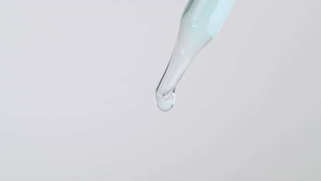 close up of dropper pipette tip with light blue liquid dripping isolated in white background