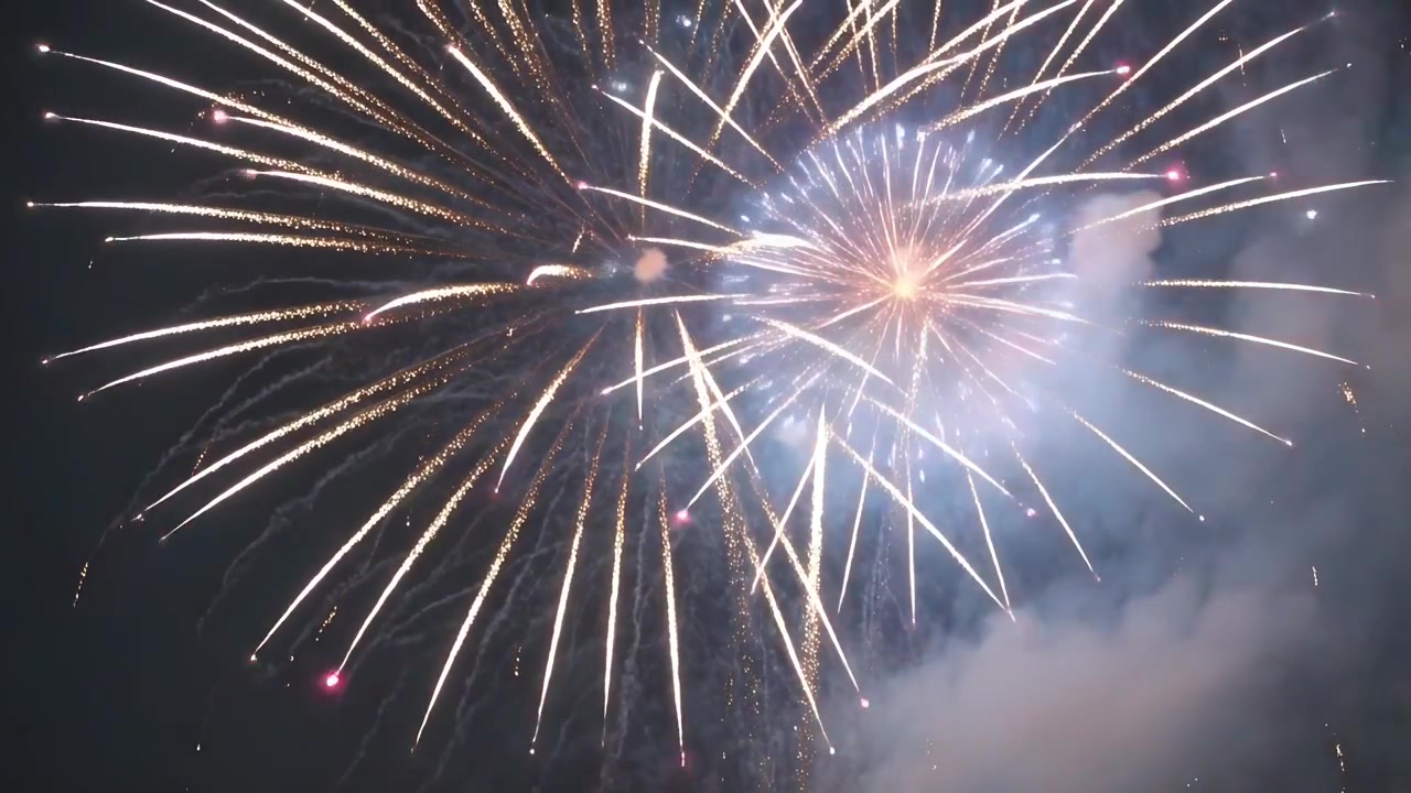 Reaching altitude, aerial firework shells detonating, filling night sky with gold trails and smoke