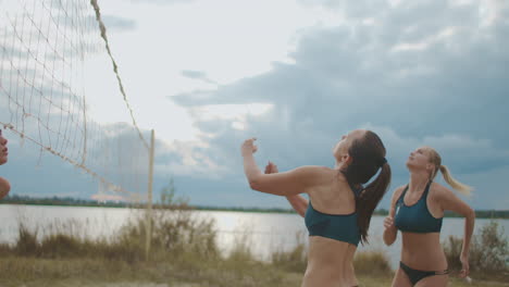 women are playing beach volleyball at summer on open court at shore of river passing and attacking